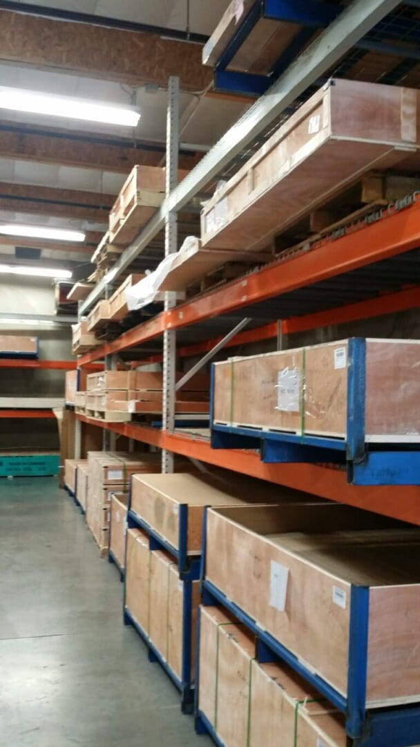 Warehouse interior with large wooden crates stacked on metal shelving units. Industrial setting with concrete floor and visible ceiling beams.