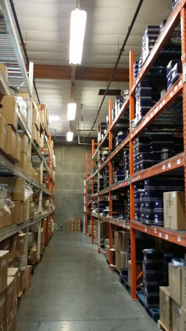 Wide aisle between tall orange metal shelves filled with assorted boxes in a well-lit warehouse.