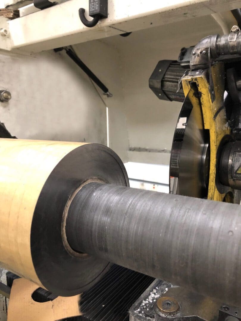 A close-up of an industrial machine with a large cylindrical metal component and paper roll in a factory setting.